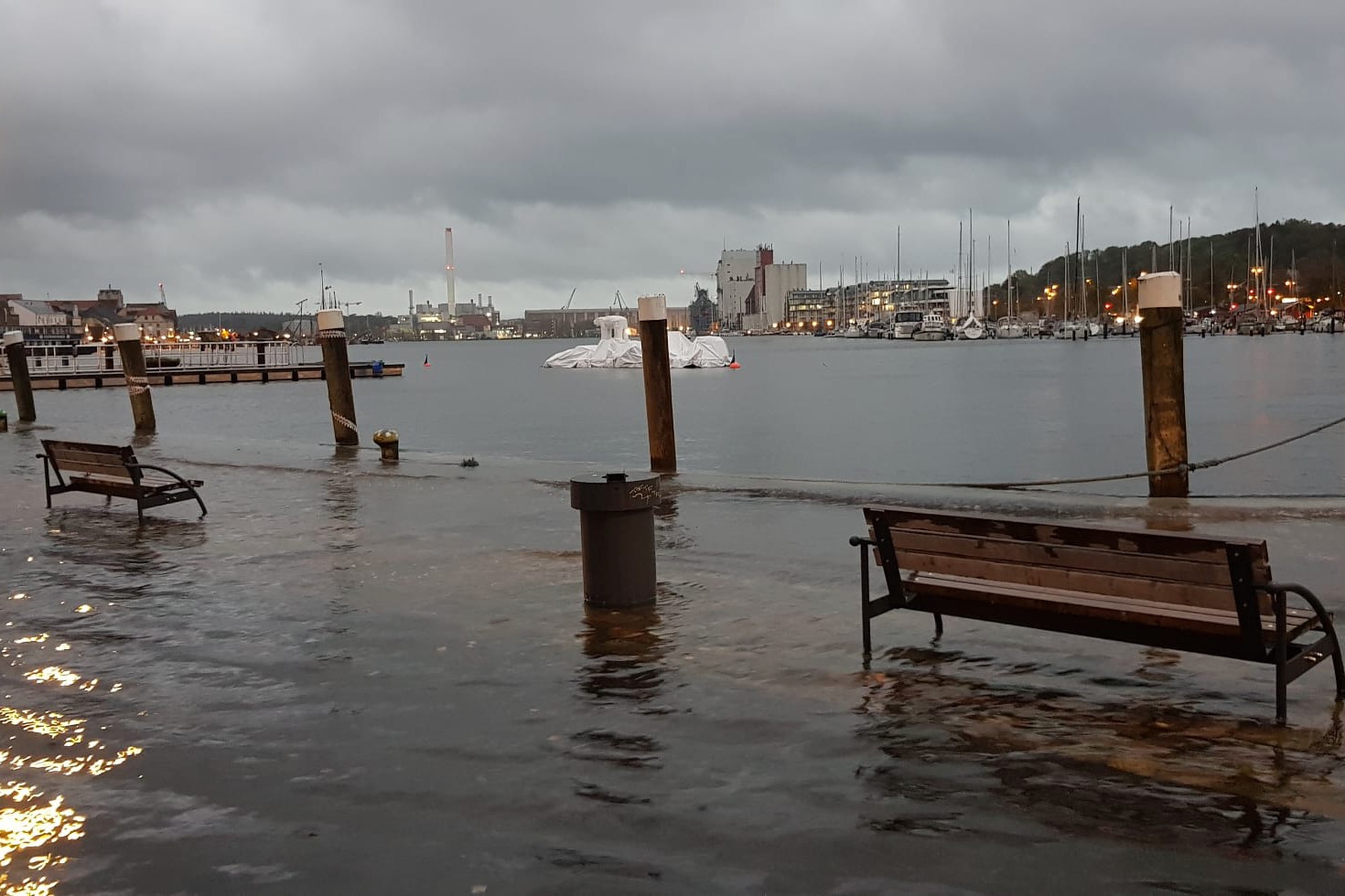 Blick über den Hafen Flensburgs. Zwei Sitzbänke im Vordergrund stehen im Wasser, das über die Kaimauer getreten ist.