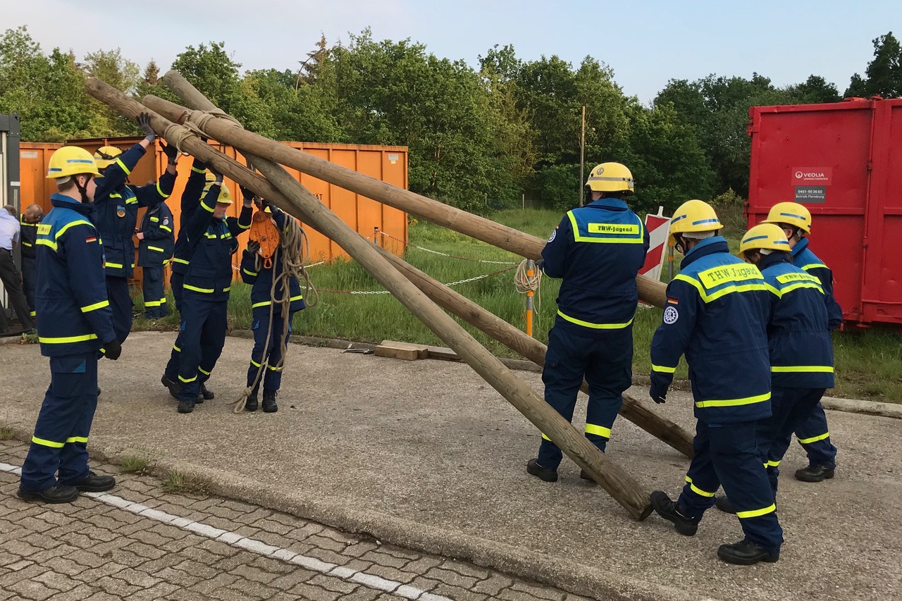 Neun Jugendliche üben den Bau eines Dreibocks aus Rundhölzern und Seilverbindung zur Hebung von Lasten.