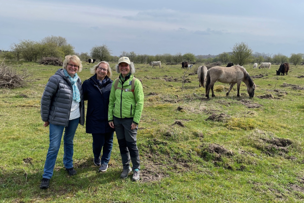 Drei Frauen stehen im Vordergrund. Dahinter grasen in Ruhe die Wildpferde.