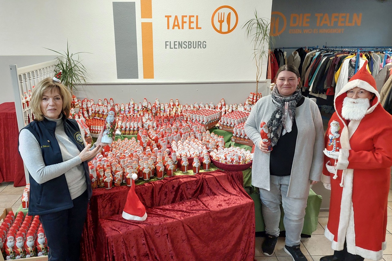 Asta Simon steht mit einem Schokoladen-Weihnachtsmann in der Hand links von weiteren 1016 Schoko-Männern, die auf Tischen aufgestellt sind. Rechts vom Tisch steht Catarina Puchleitner und neben ihr eine Person als Nikolaus verkleidet.