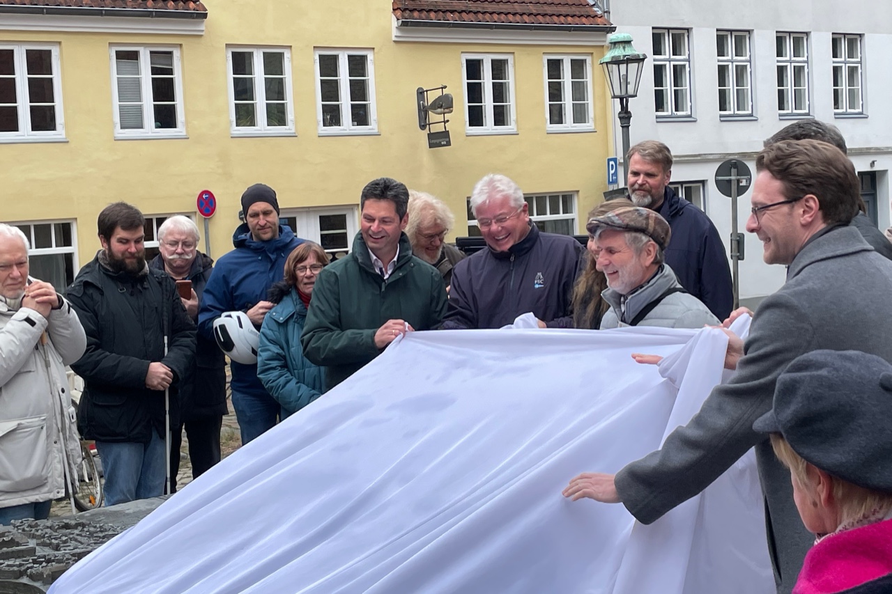 Mehrere Personen ziehen zusammen mit dem Flensburger Oberbürgermeister Dr. Fabian Geyer ein großes weißes Tuch vom Stadtmodell. Zahlreiche Zuschauer stehen im Kreis herum.