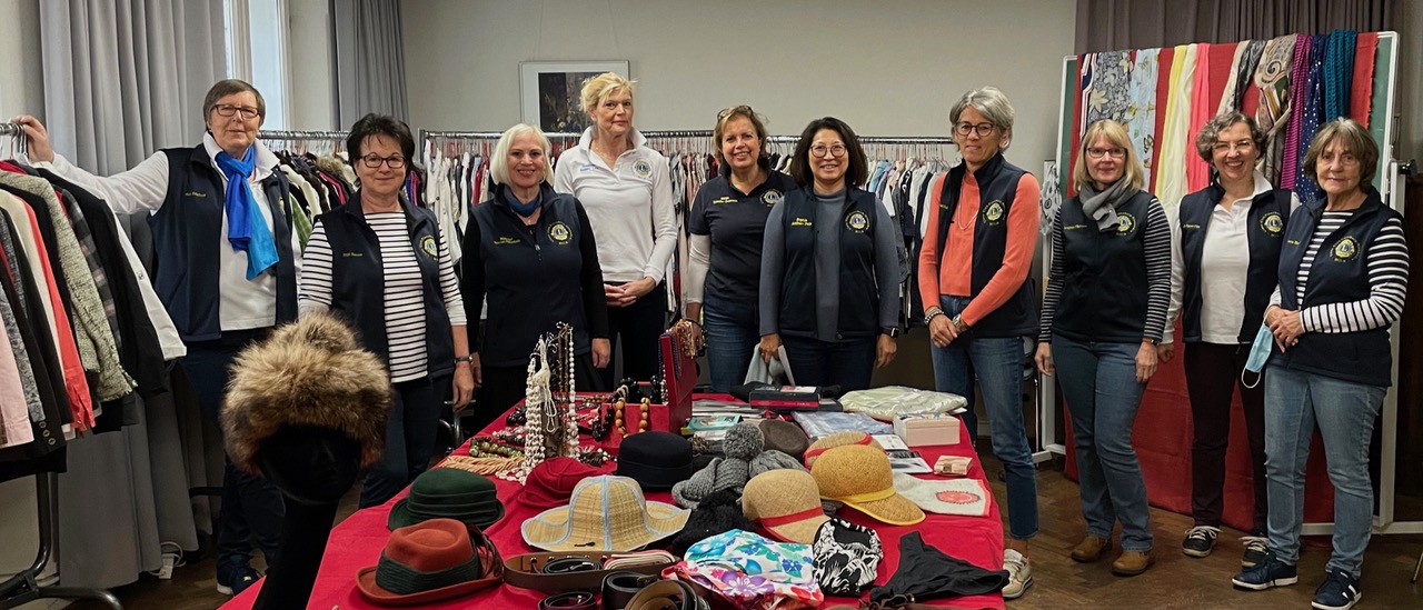 Eine Gruppe der Alexandras vor dem Start des Second-Hand-Verkauf. Im Vordergrund sind zahlreiche Hüte und Schals auf einem Tisch zum Verkauf angeboten