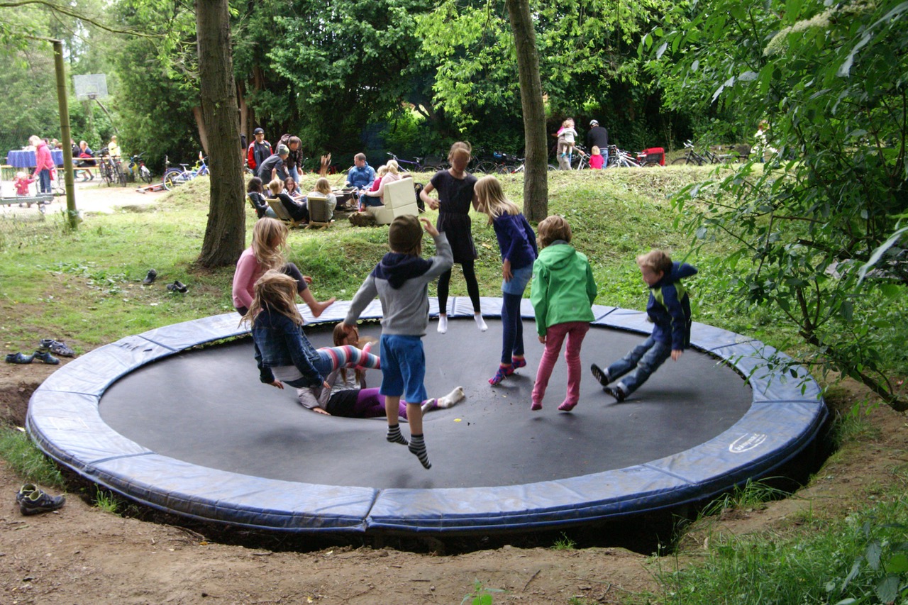 Kinder hüpfen gemeinsam auf einem großen Trampolin, das ebenerdig in den Boden eingelassen ist.