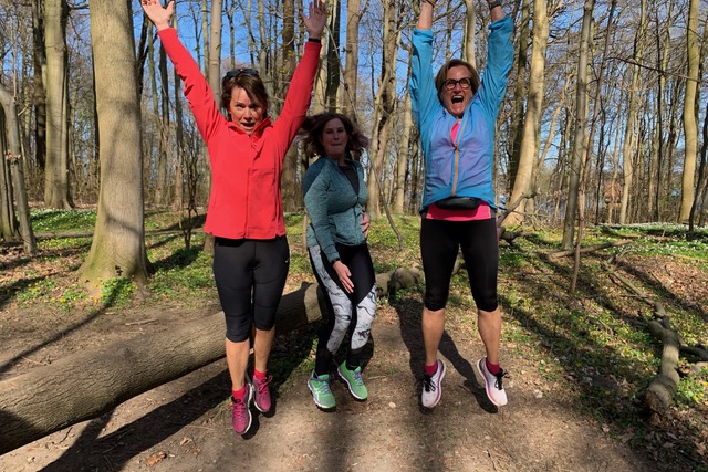 Drei Freundinnen springen mit ausgestreckten Armen im Wald in die Höhe