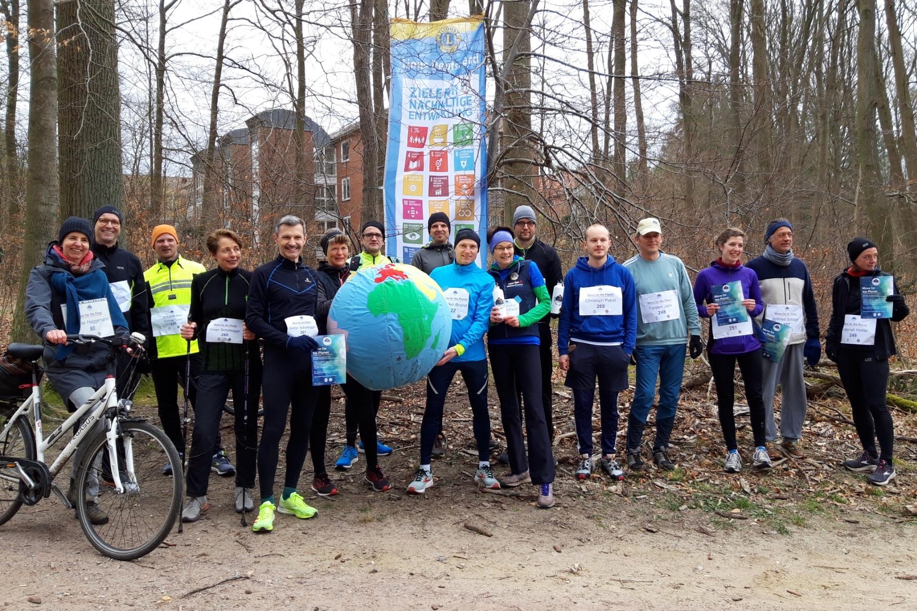 Mitglieder des Lions Club Lüneburg-Ilmenau treffen sich im Wald zum gemeinsamen Lauf. Für das Foto halten Sie eine große Weltkugel, einen Wasserball in die Höhe.