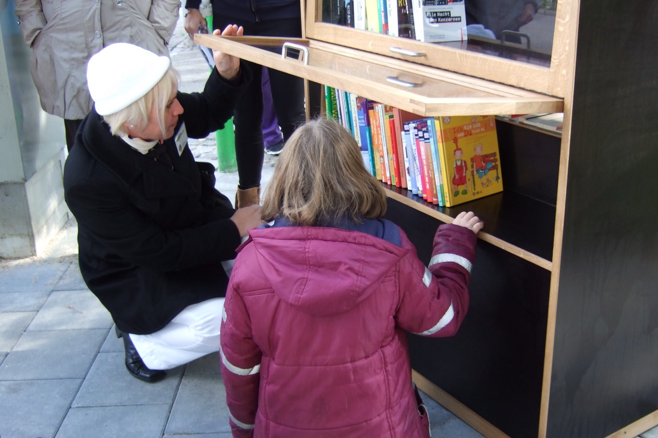 Eine Lionsfreundin zeigt zwei Kindern das Angebot in den unteren Regalen