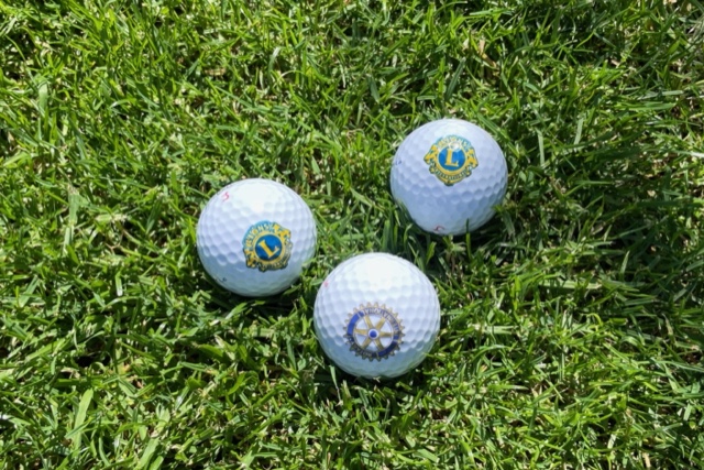 Drei Golfbälle mit den Rotary- und Lions-Logo auf dem Rasen