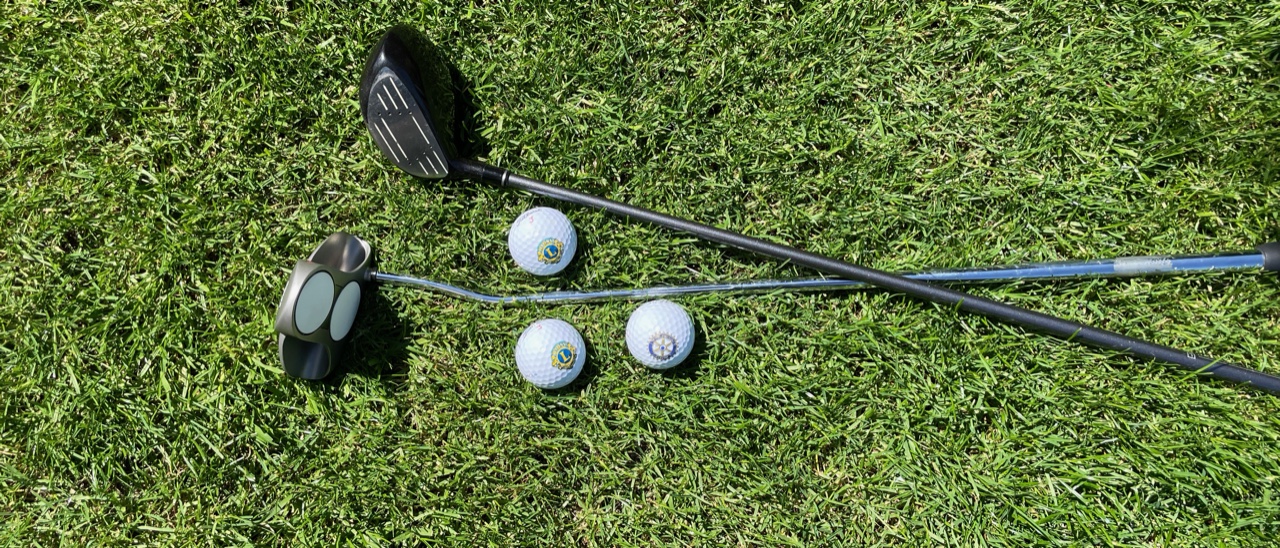Zwei Golfschläger und drei Golfbälle mit dem Rotary- und Lions-Logo auf dem Rasen